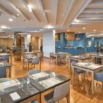 Restoranas su šviesiomis kėdėmis ir stikliniais stalais